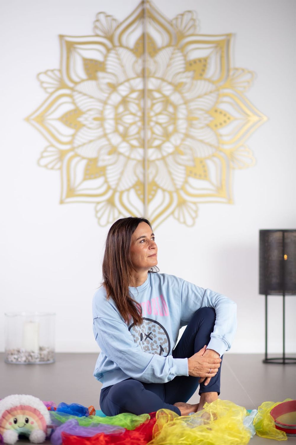 Patricia sitzt im Yogaraum unter einem goldenen Mandala und lächelt