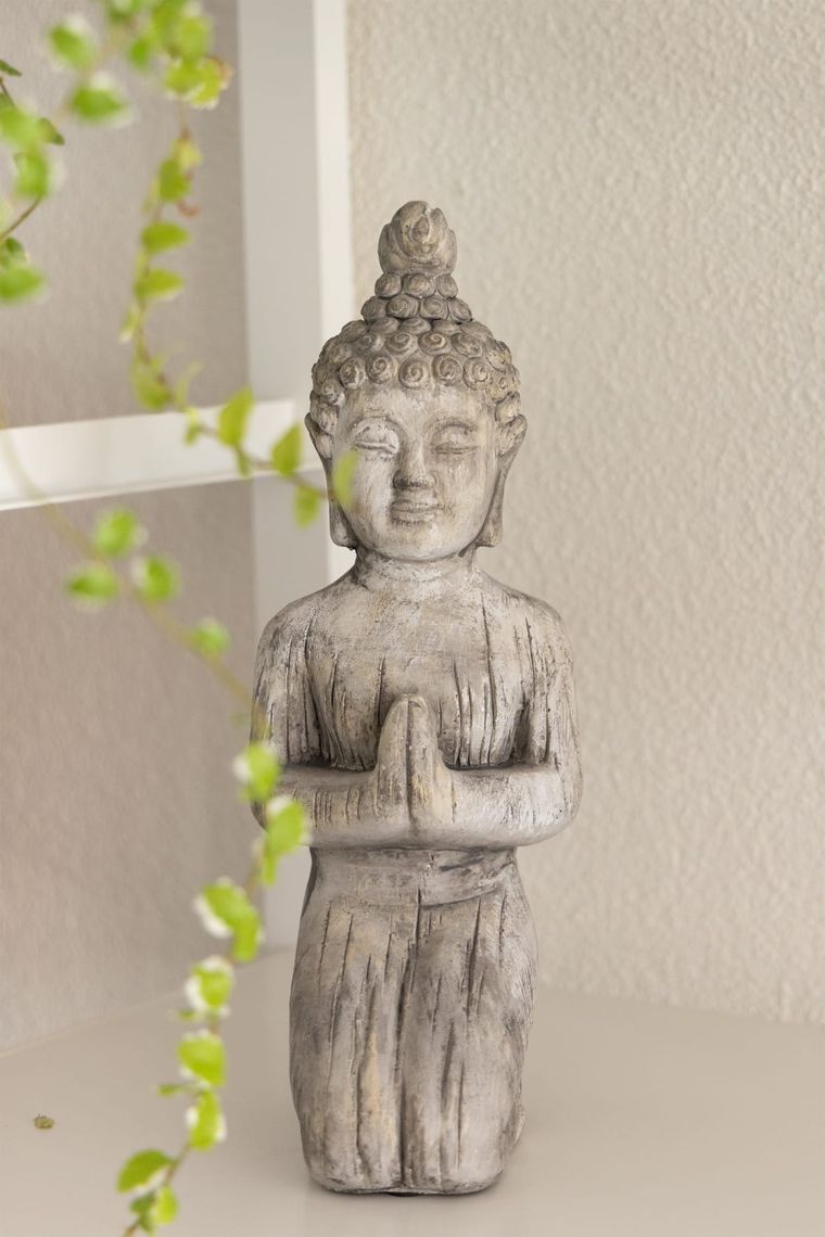 Kleine Buddha-Figur aus Stein neben einer Grünpflanze