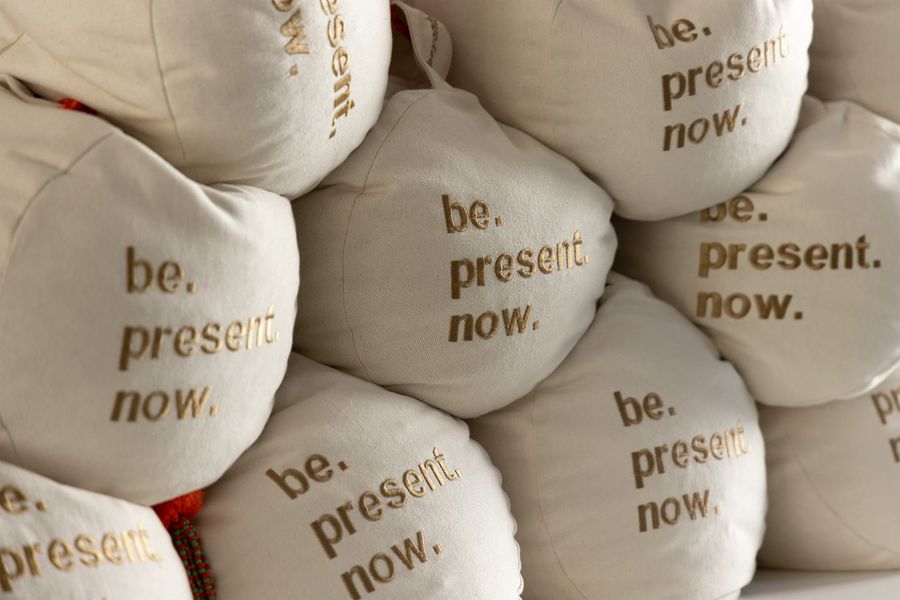 Gestapelte Meditationskissen mit der Aufschrift «be. present. now.»