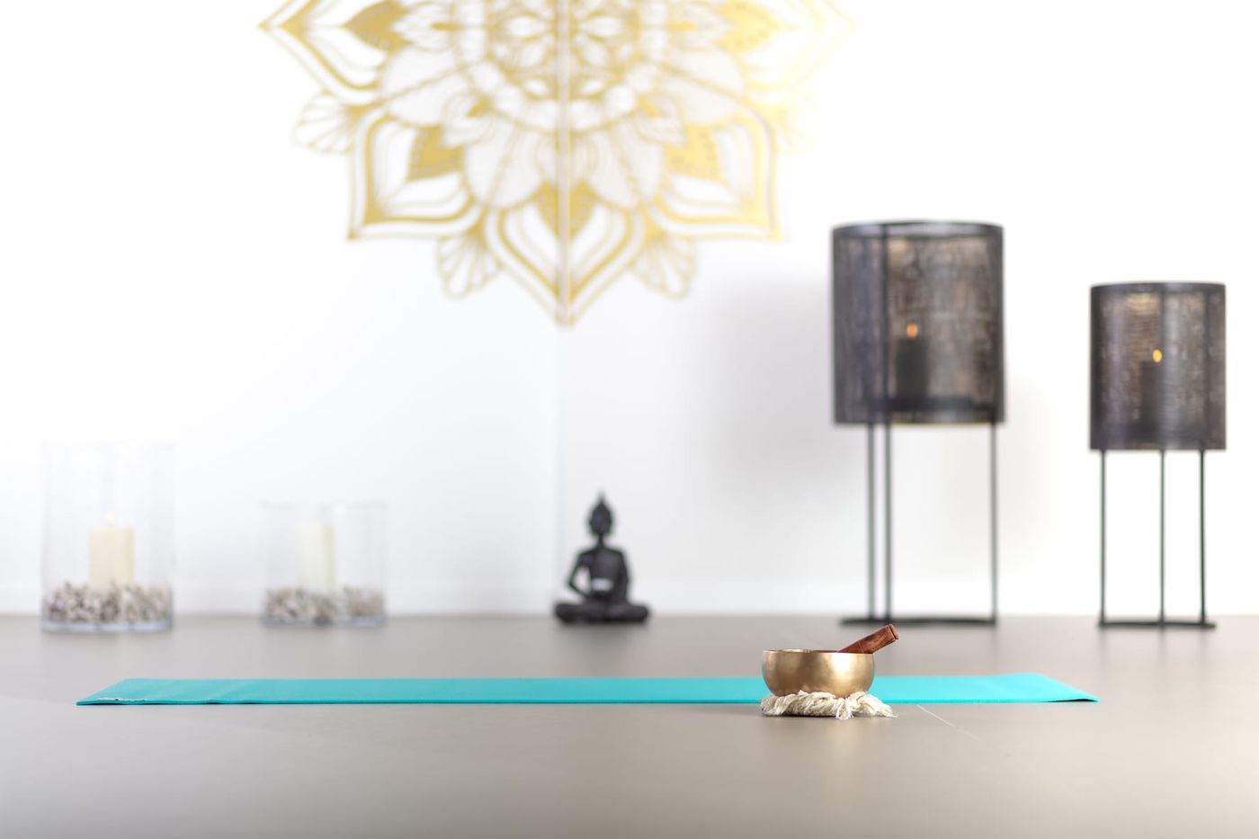 Heller Yogaraum mit goldenem Mandala an der Wand, Laternen und einer Yogamatte mit Klangschale